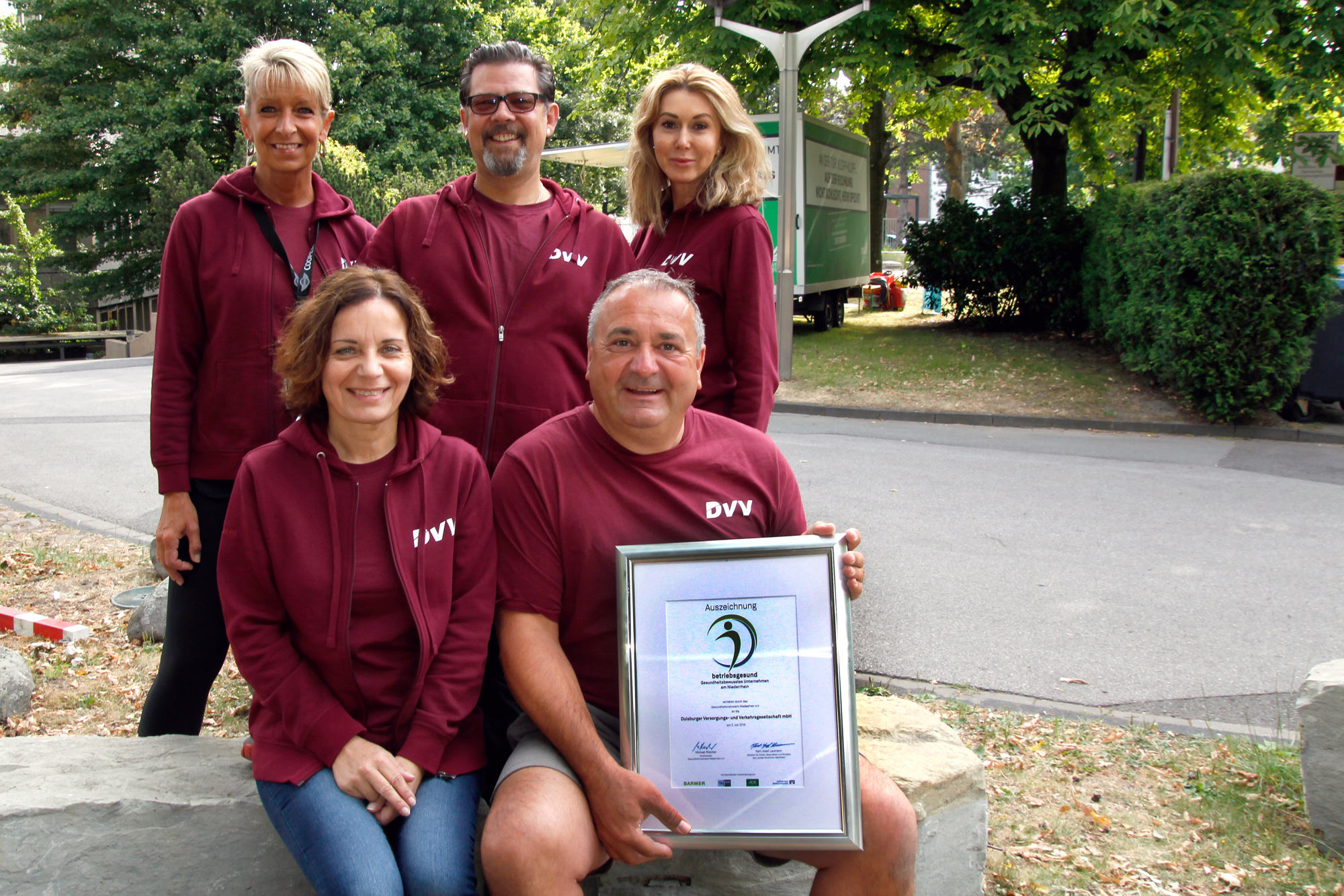Das Team des Betrieblichen Gesundheitsmanagements der DVV mit Urkunde zur Auszeichnung, Gruppenfoto im Freien.
