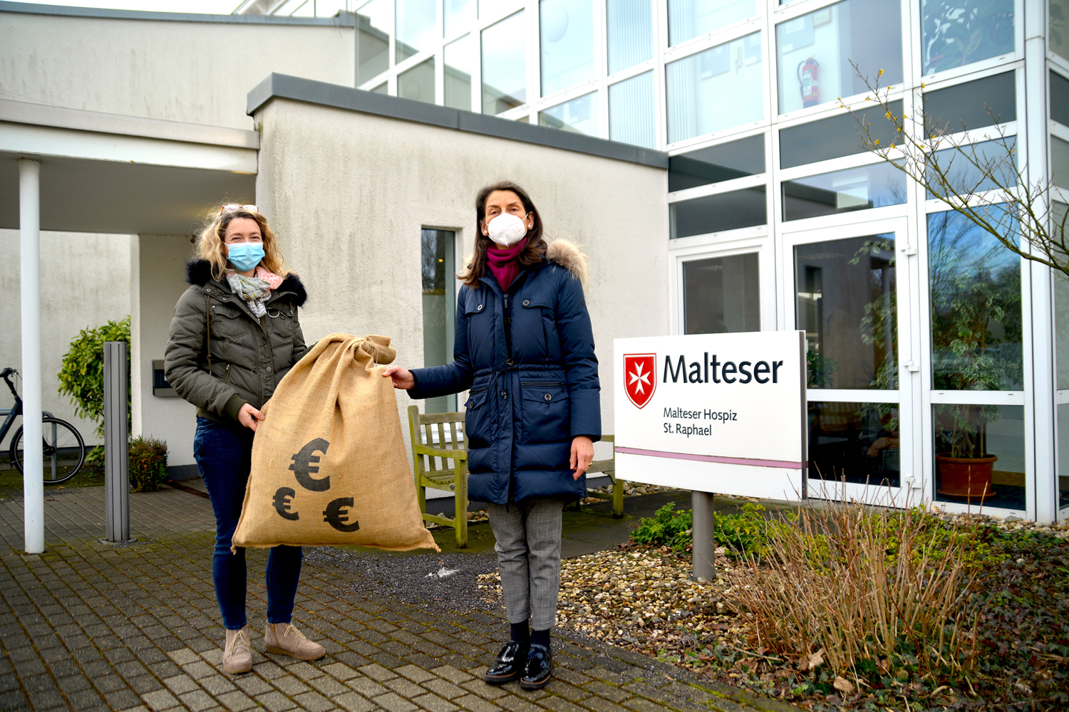 Zwei Frauen übergeben vor dem Hospizzentrum St. Raphael einen großen Sack mit Euro-Zeichen als Restcentspende.