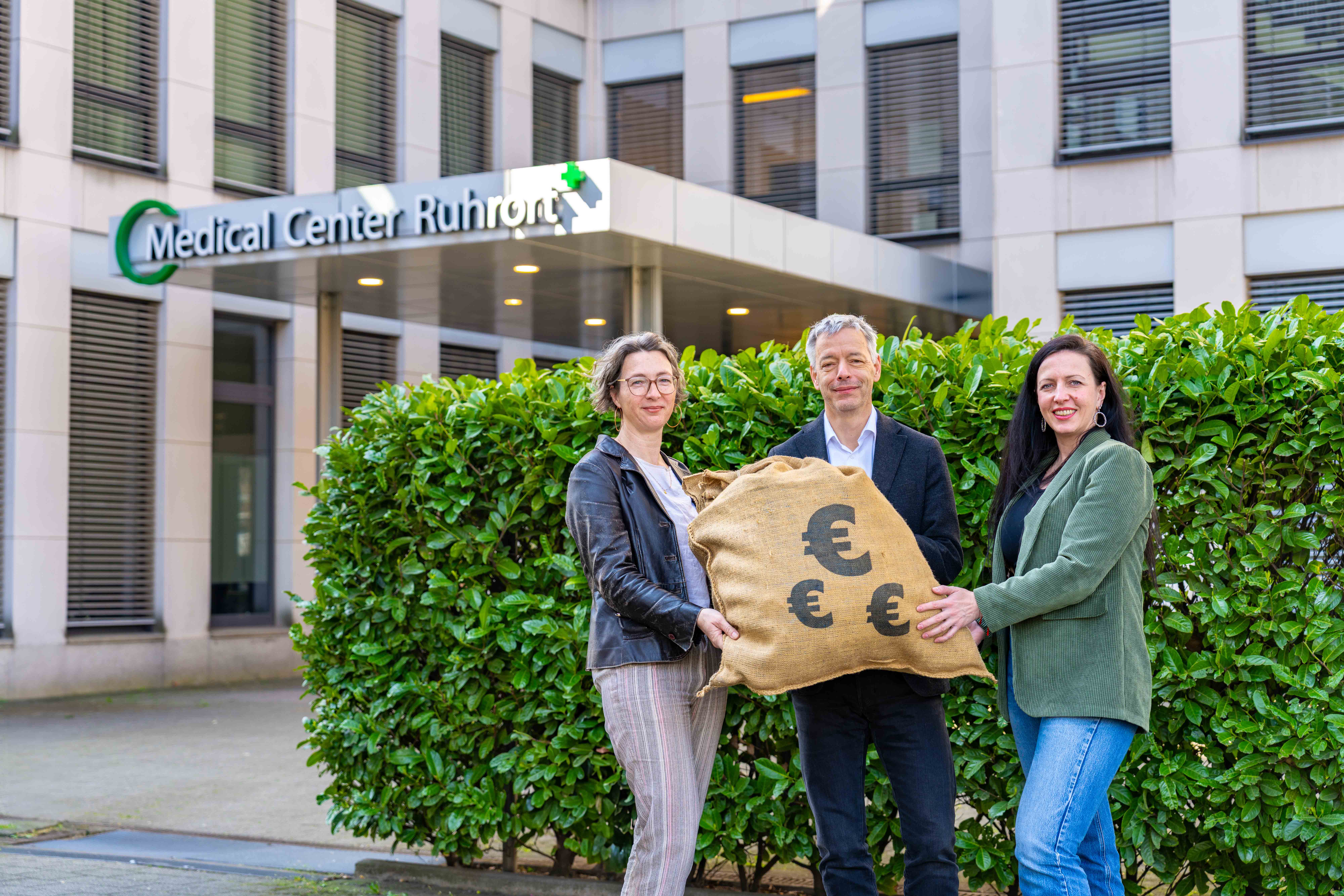 Tanja Hake übergibt prall gefüllten Restcentsack an Vertreterinnen des KipsE-Netzwerks vor dem Medical Center Ruhrort
