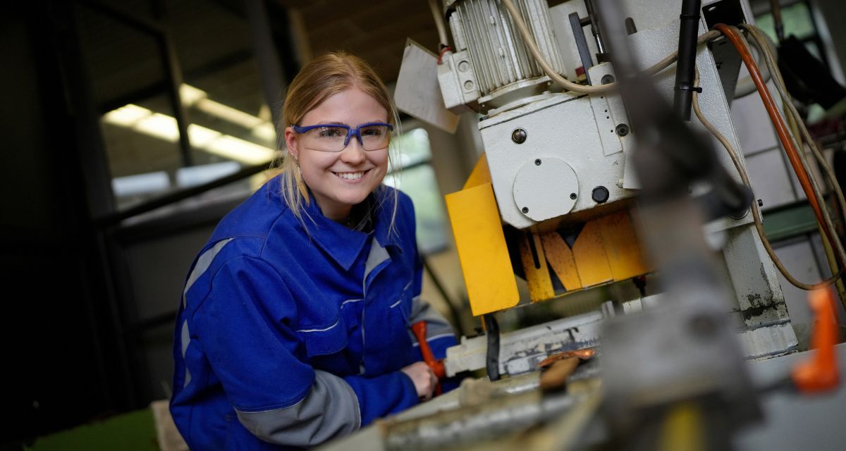 Auszubildende in blauer Schutzkleidung an einer Werkmaschine